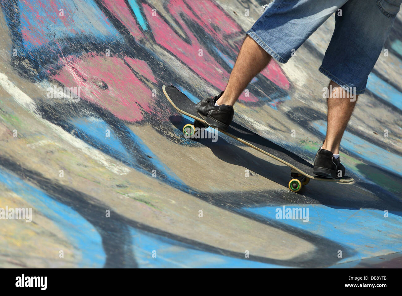 Ragazzo gambe su uno skateboard in un half pipe con graffiti Foto Stock