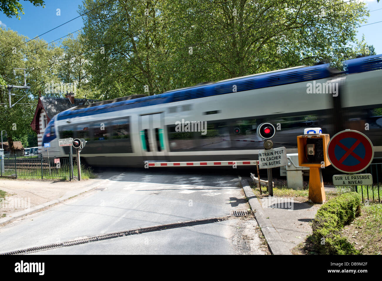 Una velocità elevata SNCF TGV alla velocizzazione, movimento sfocati attraverso un incrocio ferroviario con le barriere verso il basso e la luce rossa ACCESA, Francia Foto Stock