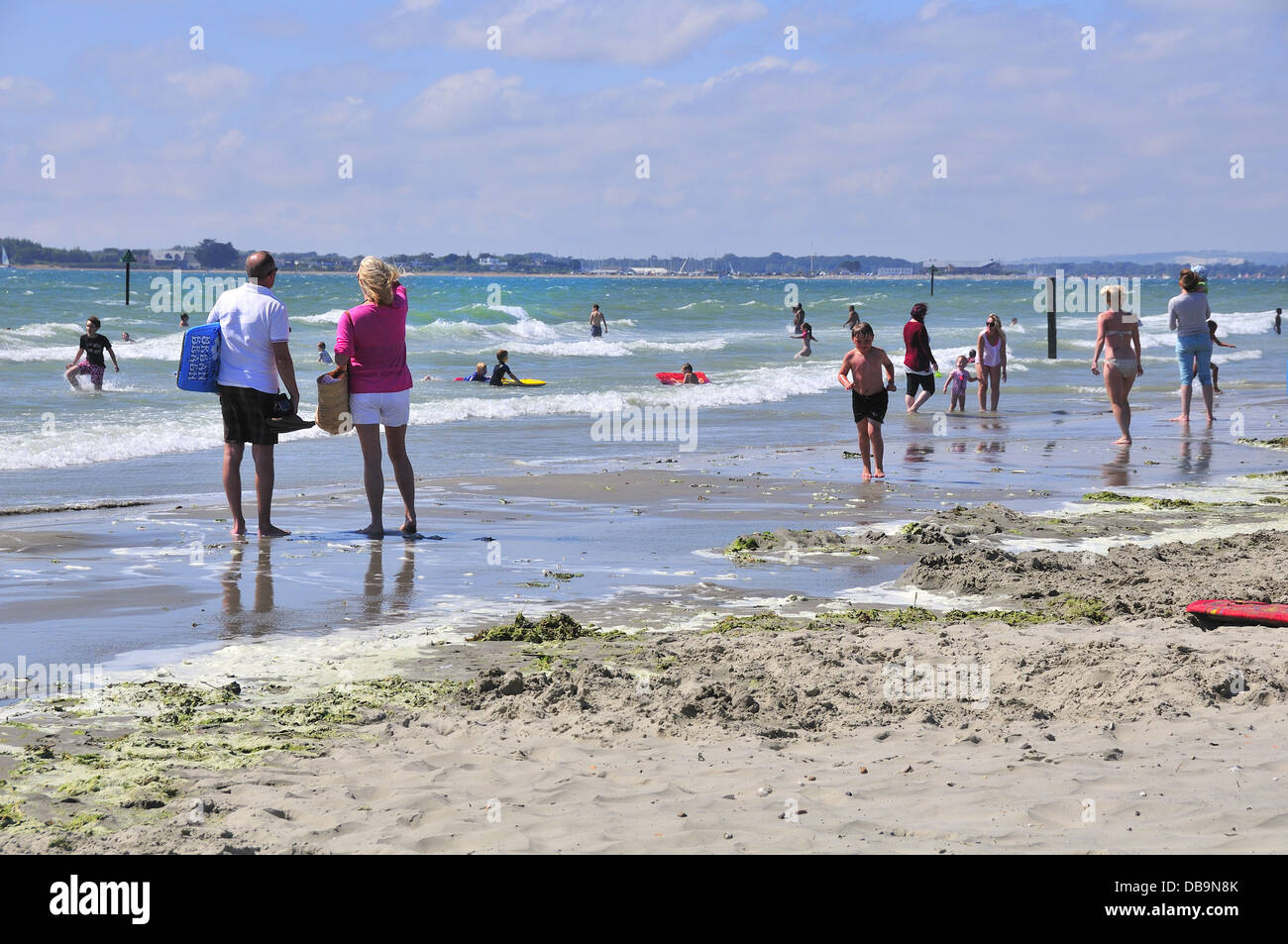 Coppia con nuotatori di sunny West Wittering spiaggia Bandiera Blu, nr. Chichester, West Sussex, Regno Unito con Hayling Island in distanza Foto Stock