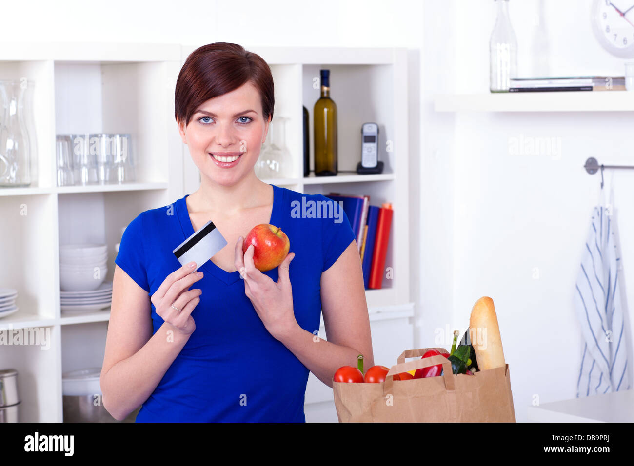 Donna con carta di credito e la borsa per la spesa in cucina a casa Foto Stock