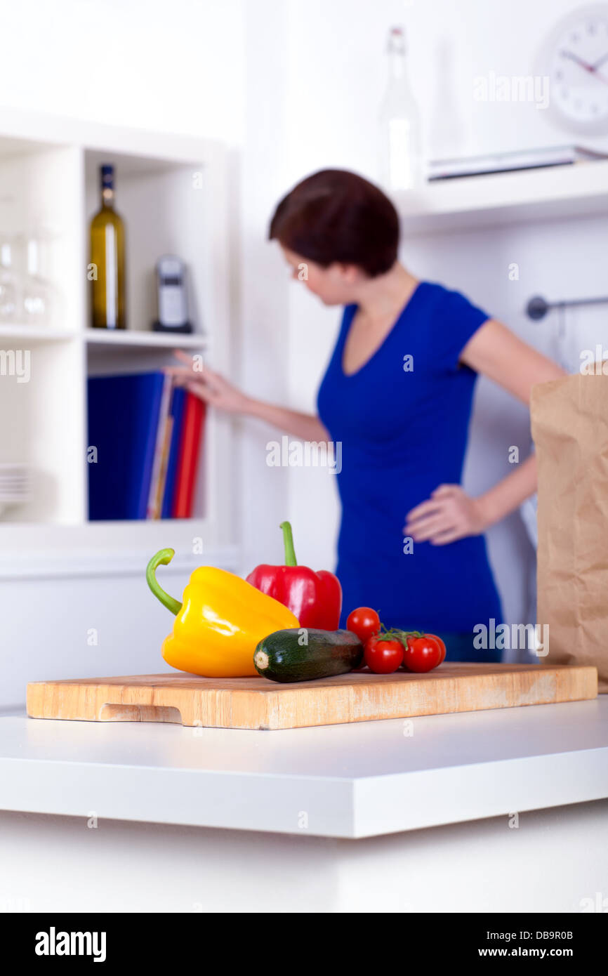 Scompattato i generi alimentari in cucina e una donna presso i ricettari Foto Stock