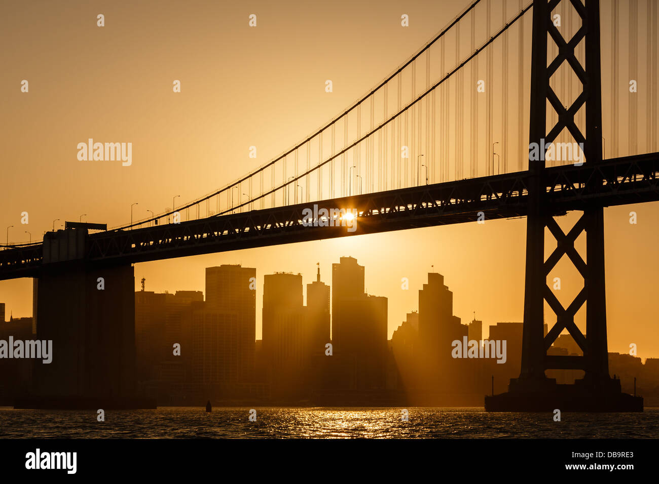 La luce del sole dorata illumina il ponte della baia e i grattacieli del lungomare di San Francisco Foto Stock