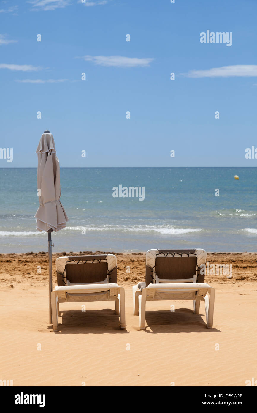 Non occupato due sedie a sdraio sulla spiaggia con ombrellone arrotolata e mare Foto Stock