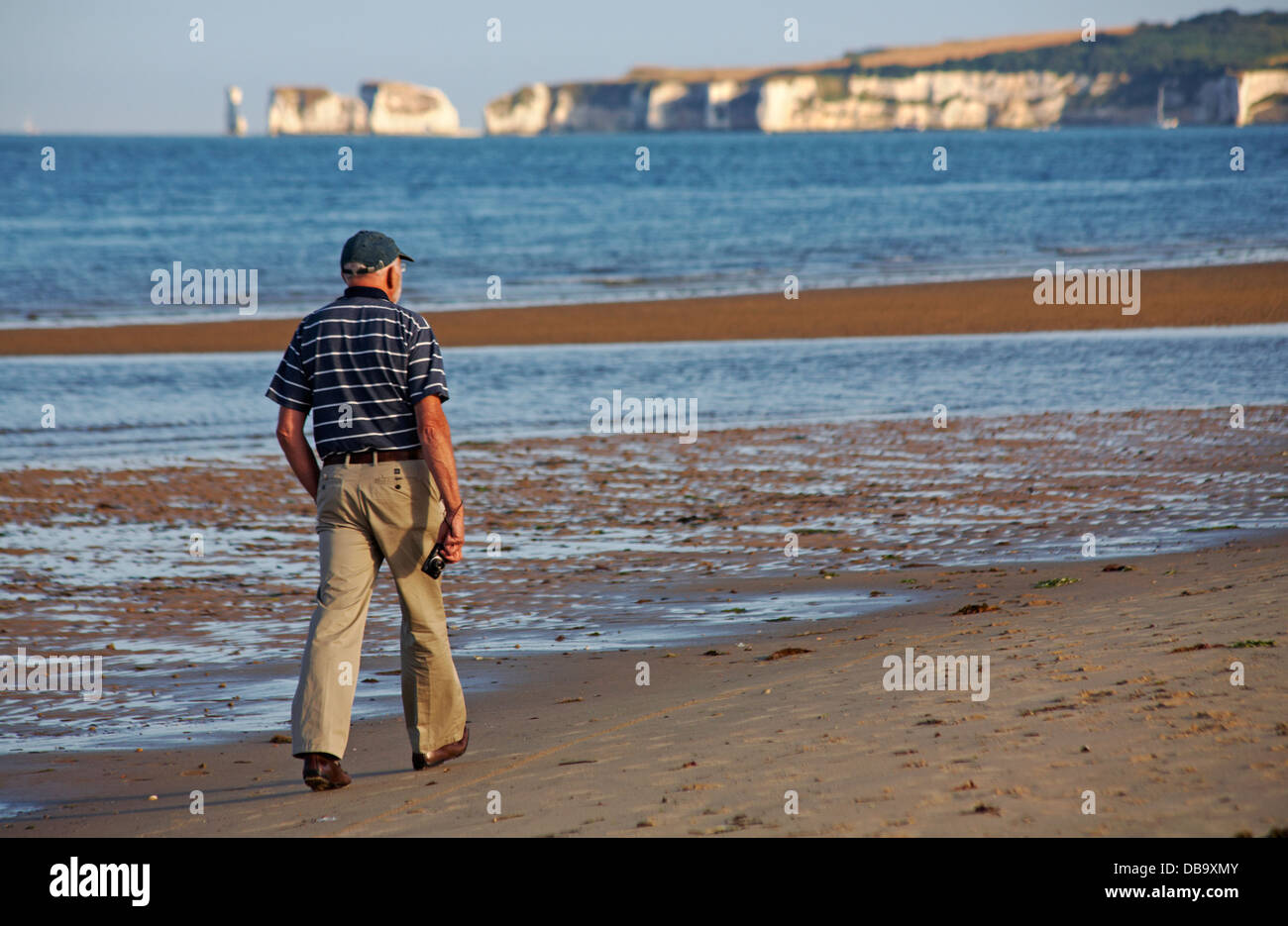 Man tenere la fotocamera a piedi lungo la spiaggia di Studland con il vecchio Harry rocce al di fuori della messa a fuoco a distanza su una sera di luglio Foto Stock