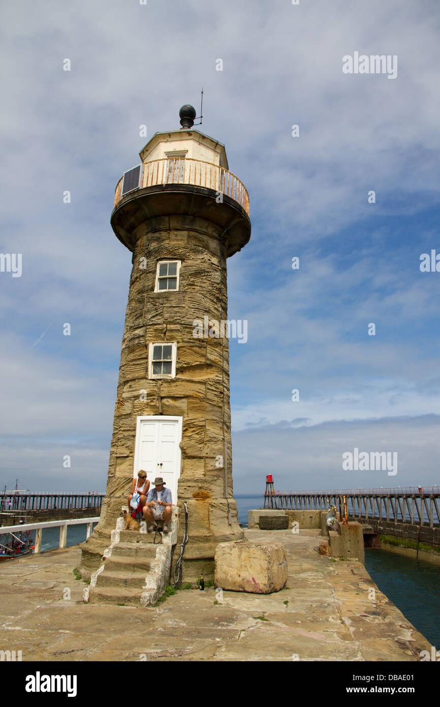 La gente seduta sui gradini al faro di Whitby ad est del molo nord Yorkshire Foto Stock