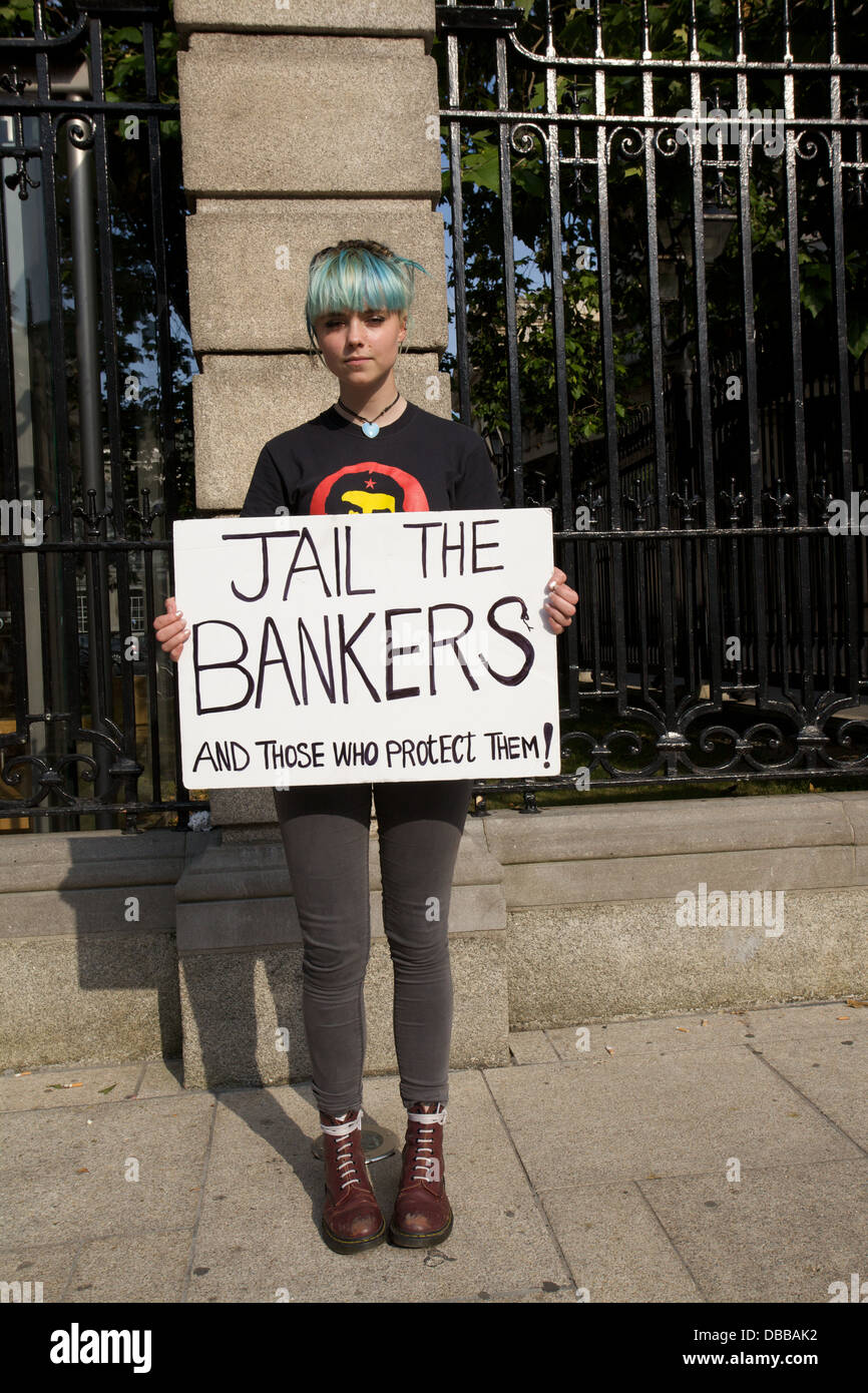 Ritratto di giovane donna in piedi in strada a Dublino, in Irlanda, con una manifestazione di protesta per targhetta della prigione di lettura dei banchieri Foto Stock