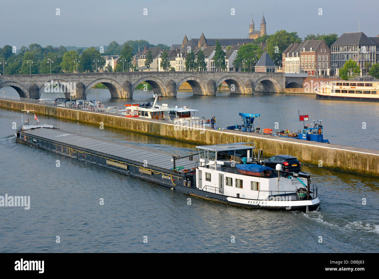 Maastricht City Waterway paesaggio urbano chiatta motoristica che si muove lungo il fiume Mosa nel canale commerciale verso il ponte ad arco di Saint Servatius Foto Stock