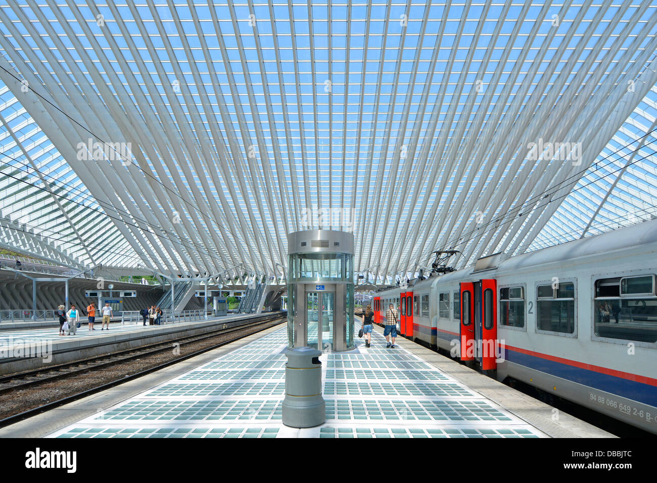 La gente sui binari del treno & giovane a piedi lungo la banchina della stazione Liège Belgio al di sotto di moderna costruzione tetto di vetro soffitto blu cielo estate giornata EU Foto Stock