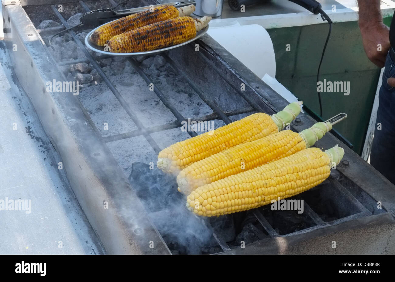 Un venditore ambulante grigliare sulla pannocchia di mais su un barbecue grill. Foto Stock