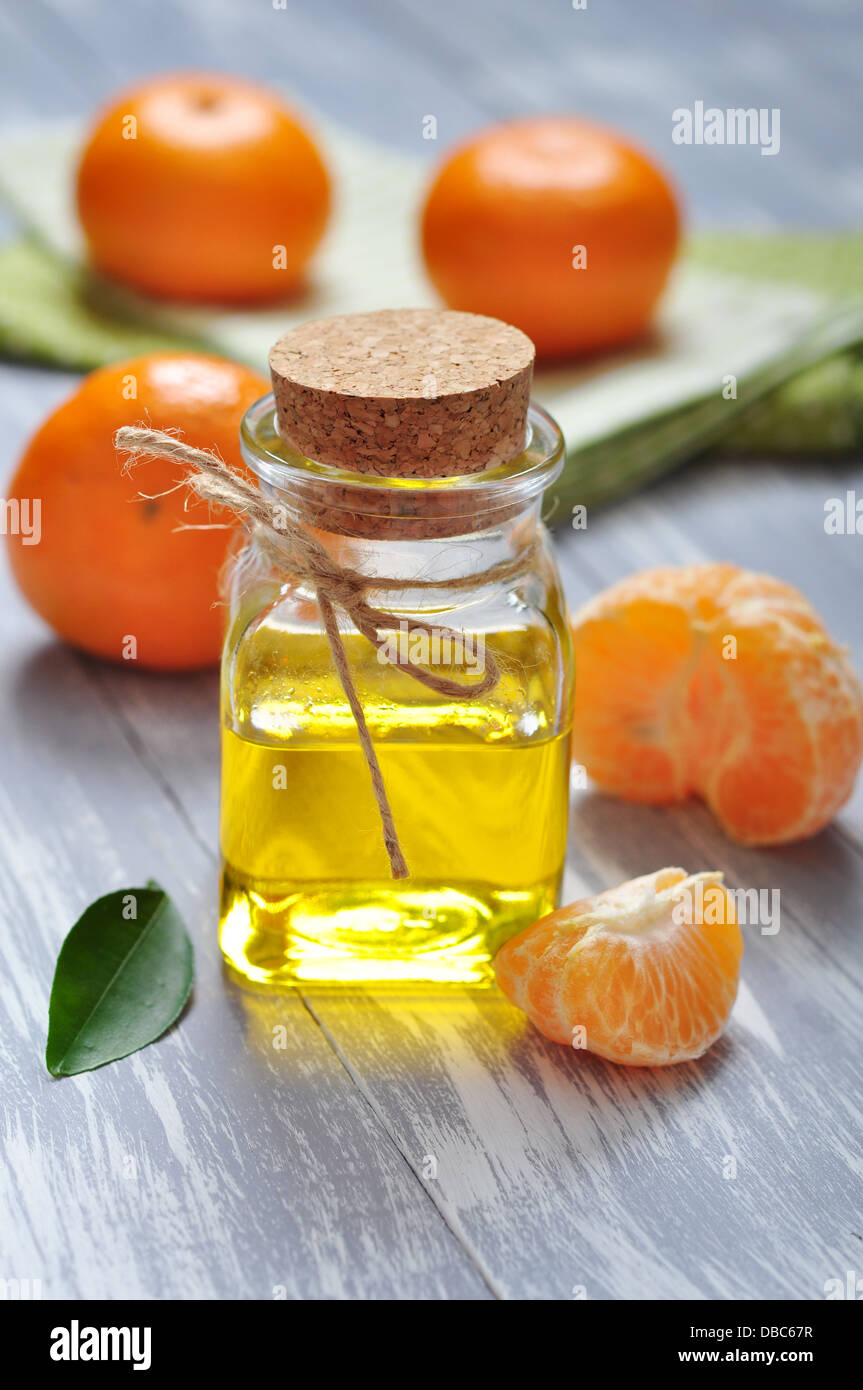 Tangerine olio in una bottiglia di vetro con fresco mandarino он sfondo di legno Foto Stock