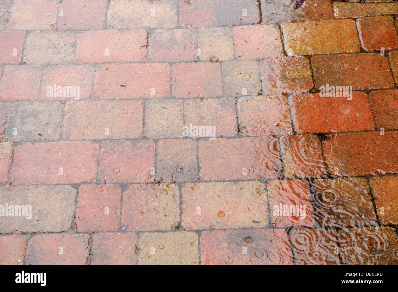 Gocce di pioggia pesante schizzi sul rustico rosso mattone pavimentazione patio nel giardino del Regno Unito con giunti poroso che agisce come superficie di acqua soakaway Foto Stock