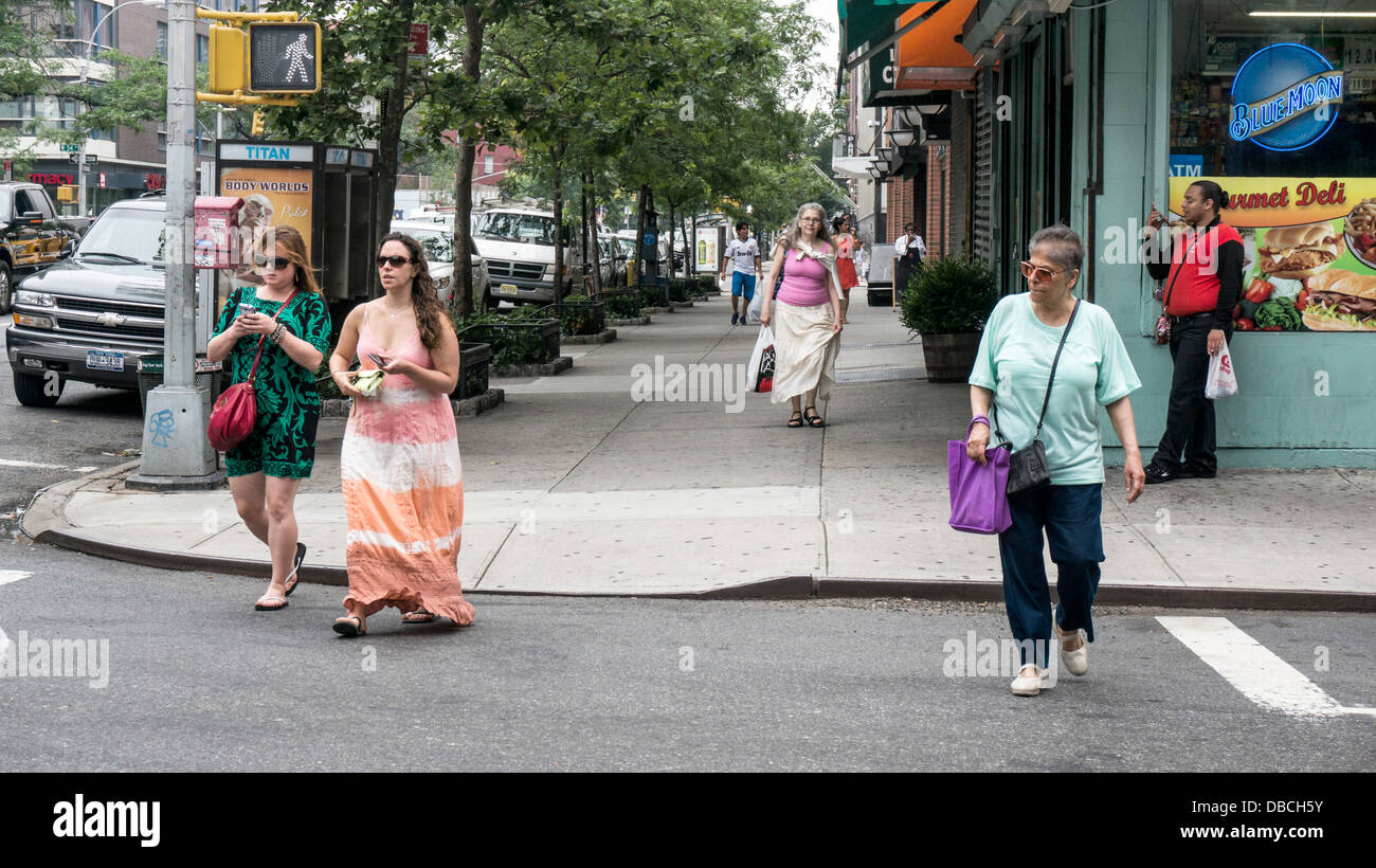 I pedoni sulla Nona Avenue su una bella giornata d'estate con diverse donne alla moda da indossare gonne lunghe Hells cucina New York Foto Stock