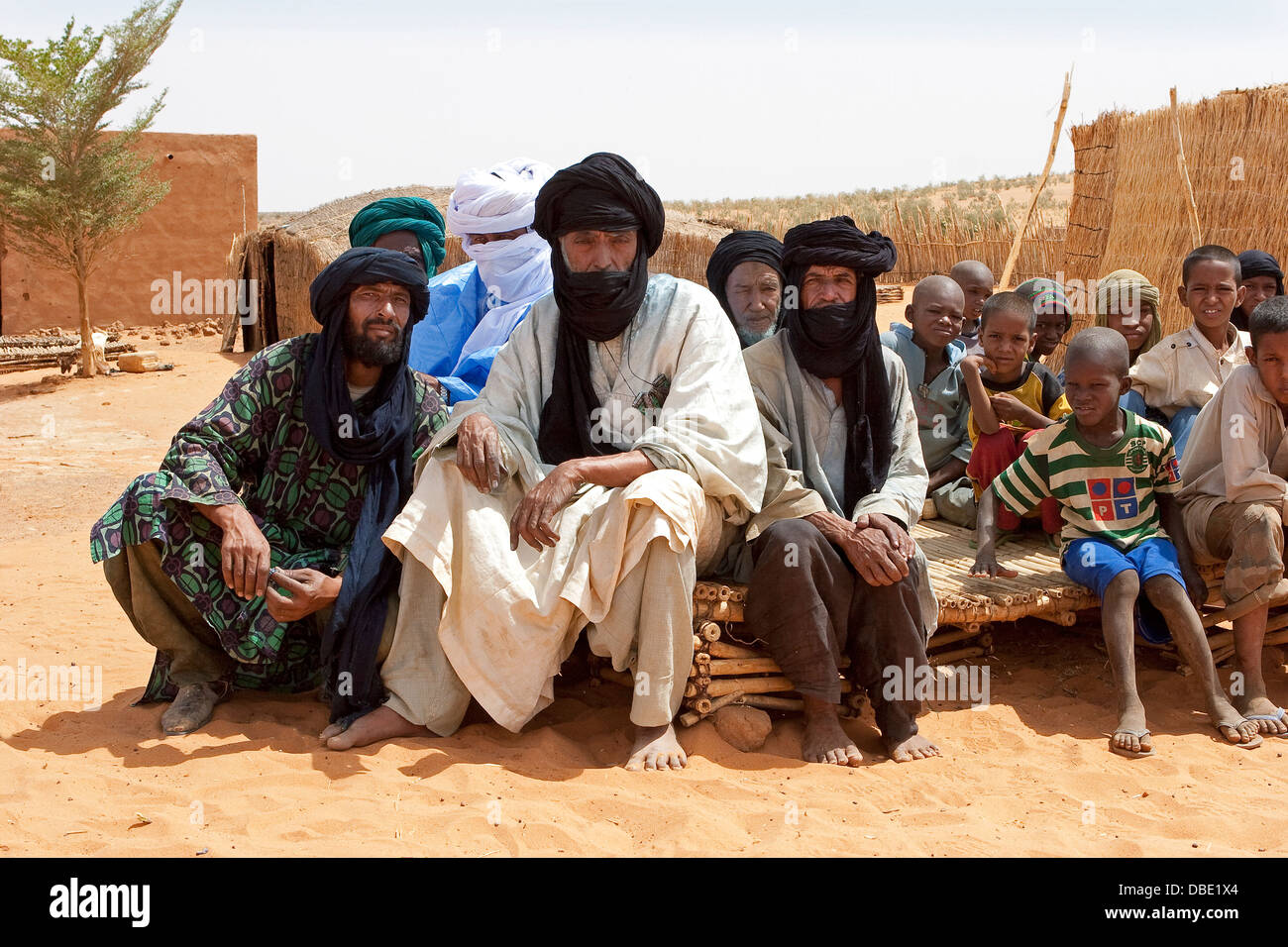 Il Tuareg capo villaggio con un gruppo di anziani e bambini in età scolare nel centro del villaggio composto, est Mali, Africa occidentale Foto Stock