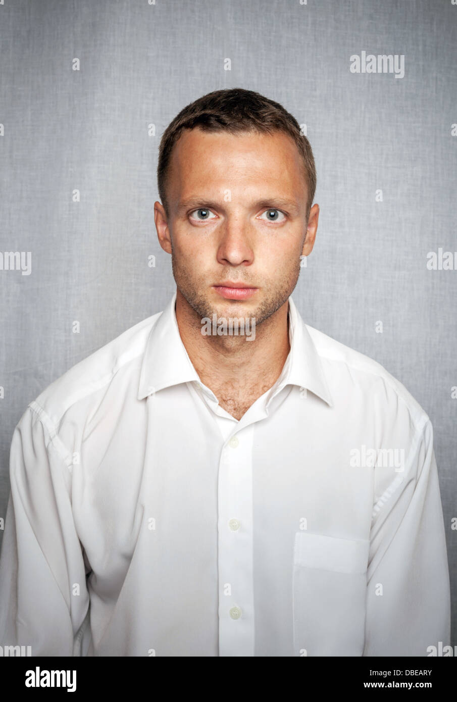 Giovane uomo gravi in maglia bianca su sfondo grigio. Ritratto in studio Foto Stock