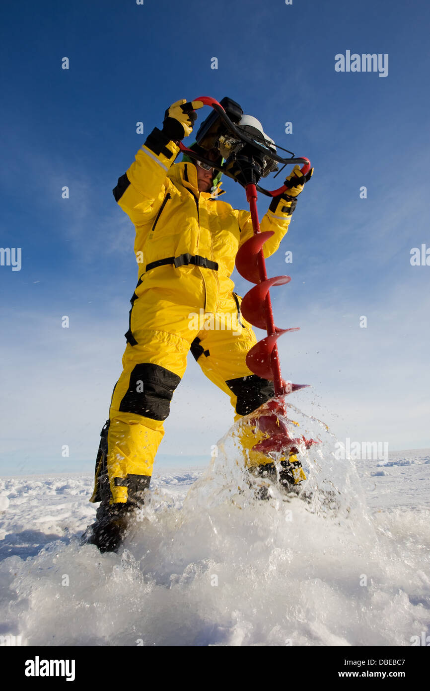 Pescatore di ghiaccio la trapanatura di un foro con una coclea di alimentazione Foto Stock
