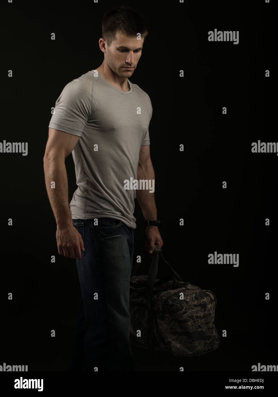 Robusto muscolare maschio caucasico indossano jeans e maglietta a maniche corte grigia che porta lo stile militare in borsa. Lasciando home / lavoro / Azienda Foto Stock