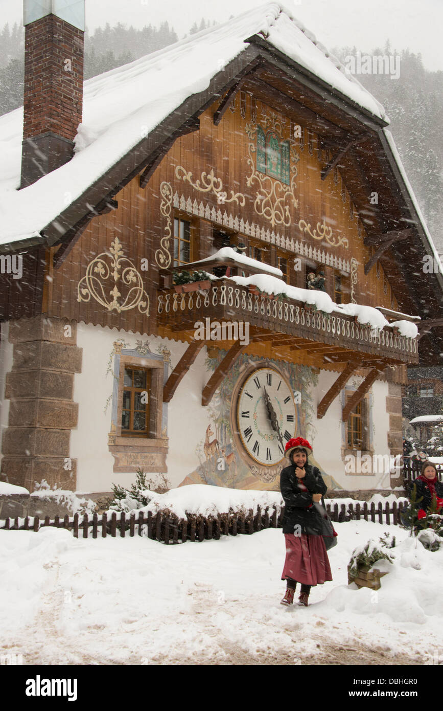 Germania, Foresta Nera, Hollsteig. Hofgut Sternen Village. Donna in 'pompom' cappello di fronte all'orologio a cucù sulla costruzione. Foto Stock