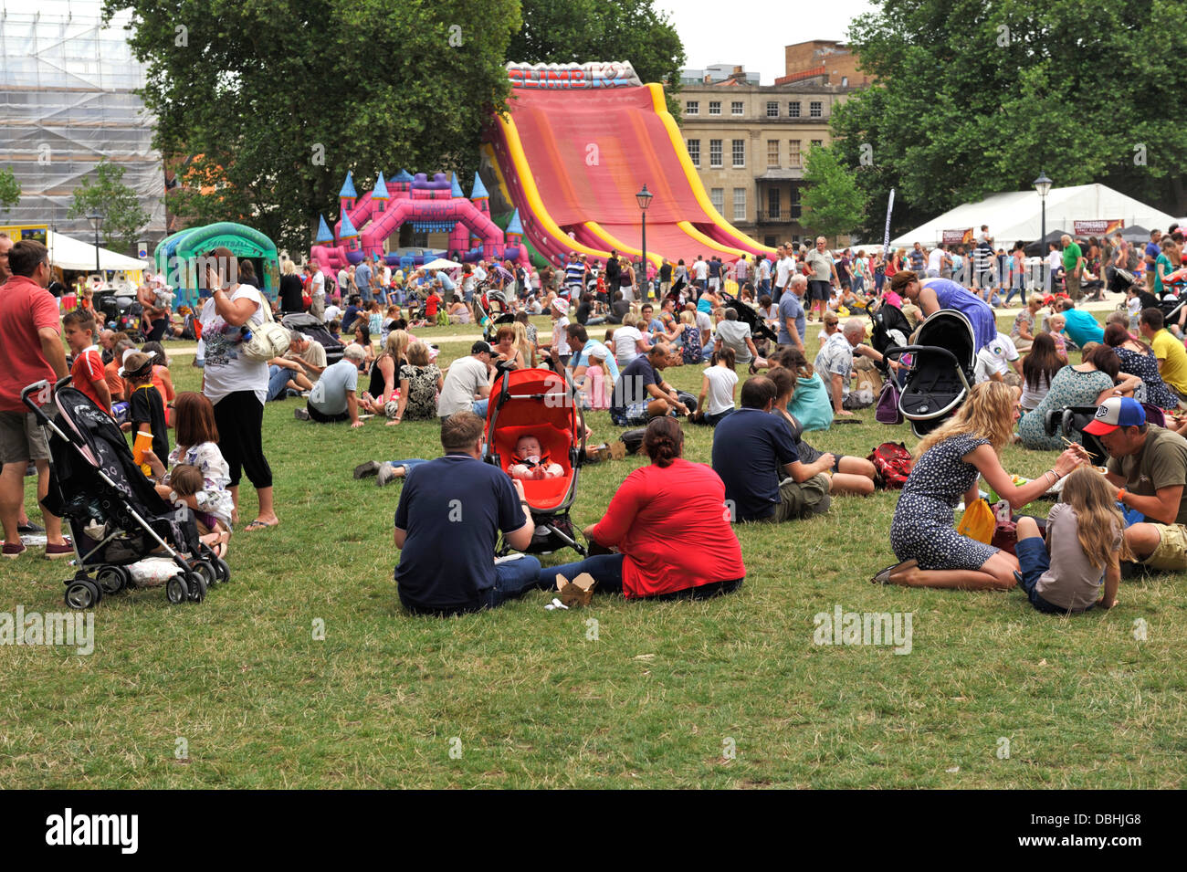 Una folla di gente che rilassante in sun a Bristol Queen Square park durante il Festival del porto con divertimenti gonfiabile in background Foto Stock