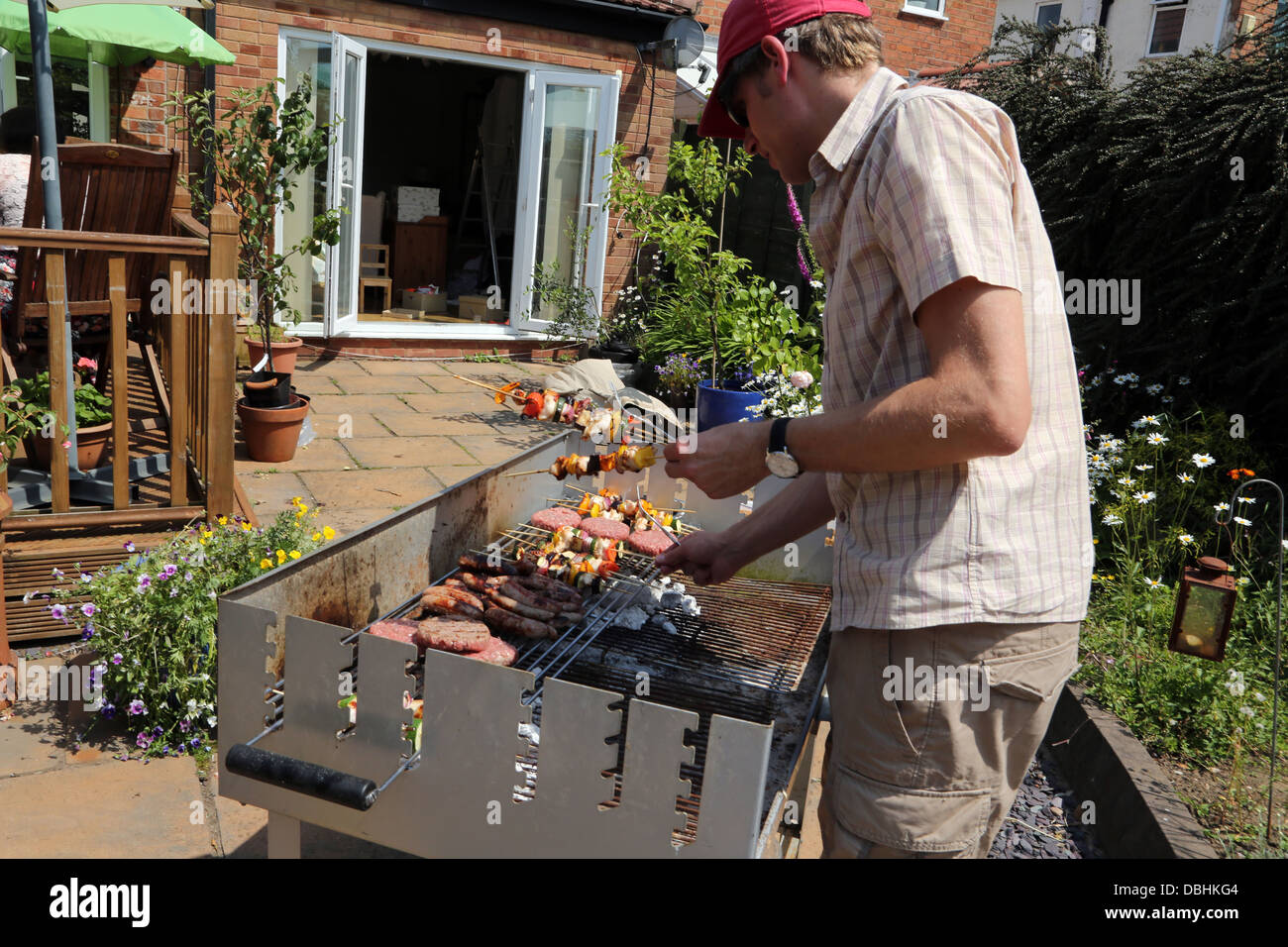 L'uomo la cottura di hamburger, spiedini e salsicce sul barbecue in giardino nei mesi estivi Birmingham West Midlands England Foto Stock