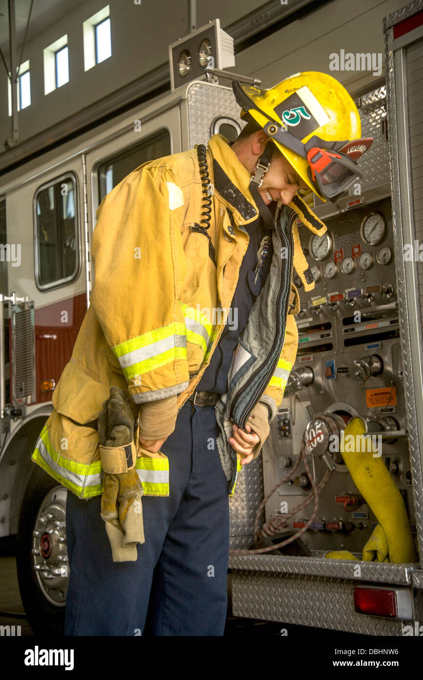 Indossa il suo casco, un giovane vigile del fuoco indossa il suo giallo giacca di sicurezza ad una firehouse in Laguna Niguel, CA. Foto Stock
