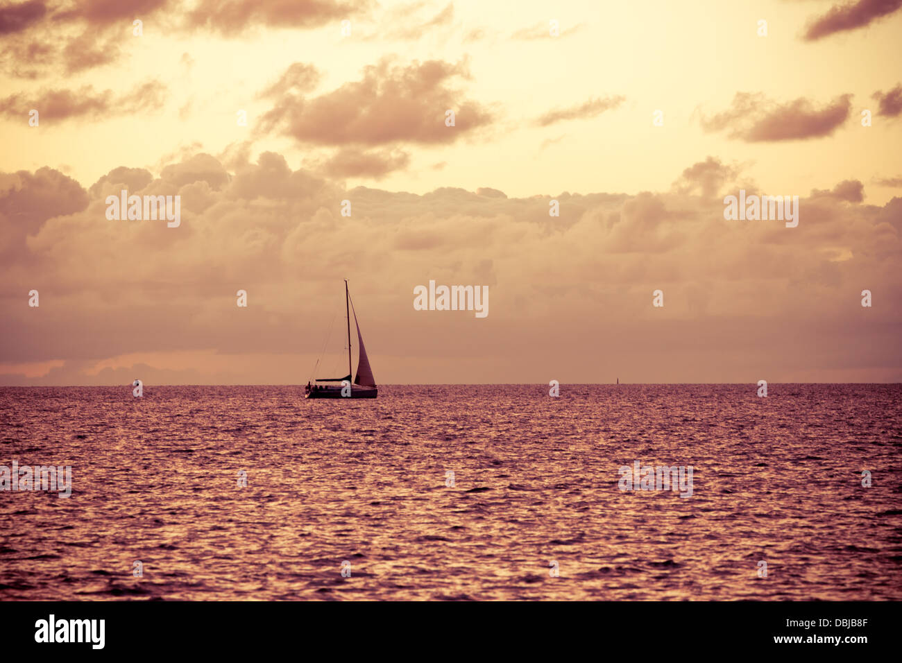 Una solitaria in barca a vela in mare aperto al tramonto, look vintage Foto Stock