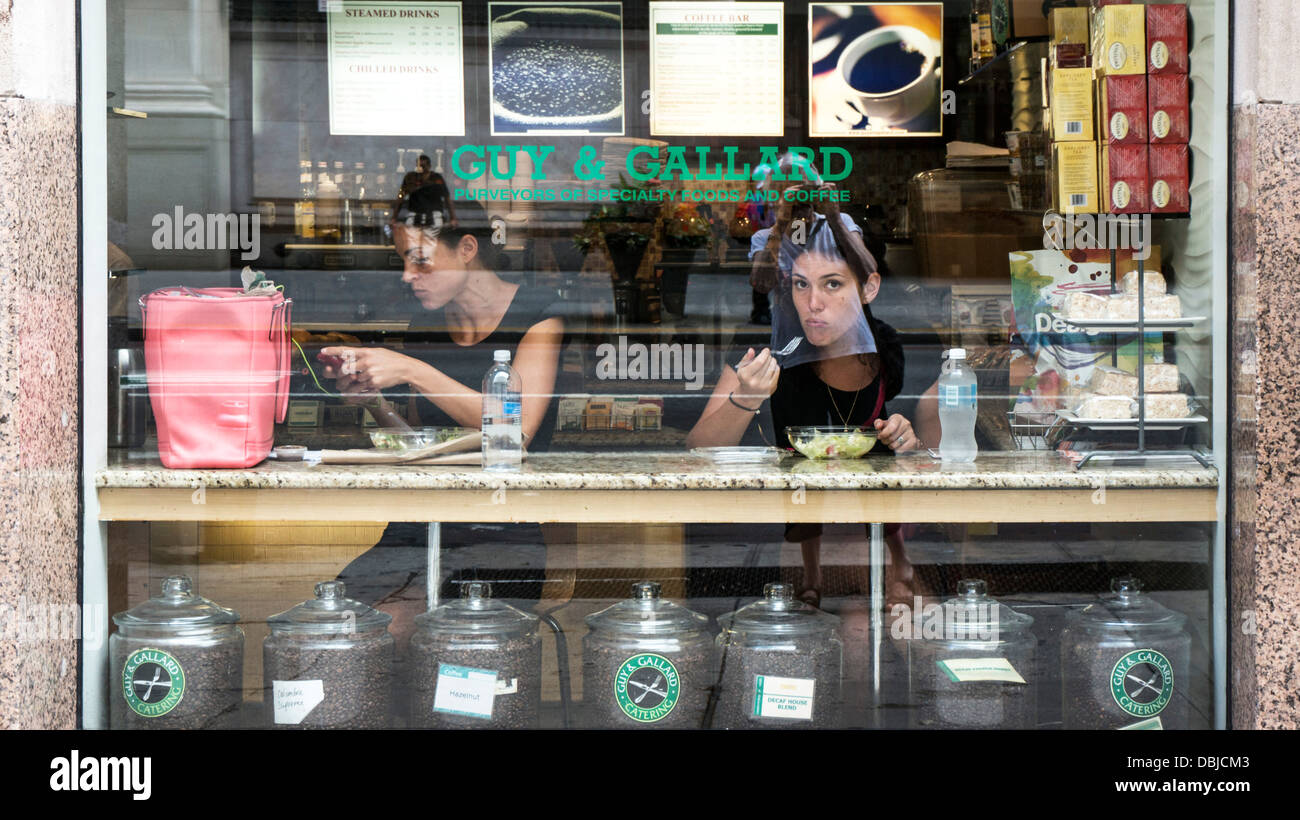 Vista sul marciapiede 2 giovani donne di business di mangiare il pranzo all'interno in corrispondenza della finestra contatore di esclusivo coffee bar East 34th street Manhattan Foto Stock