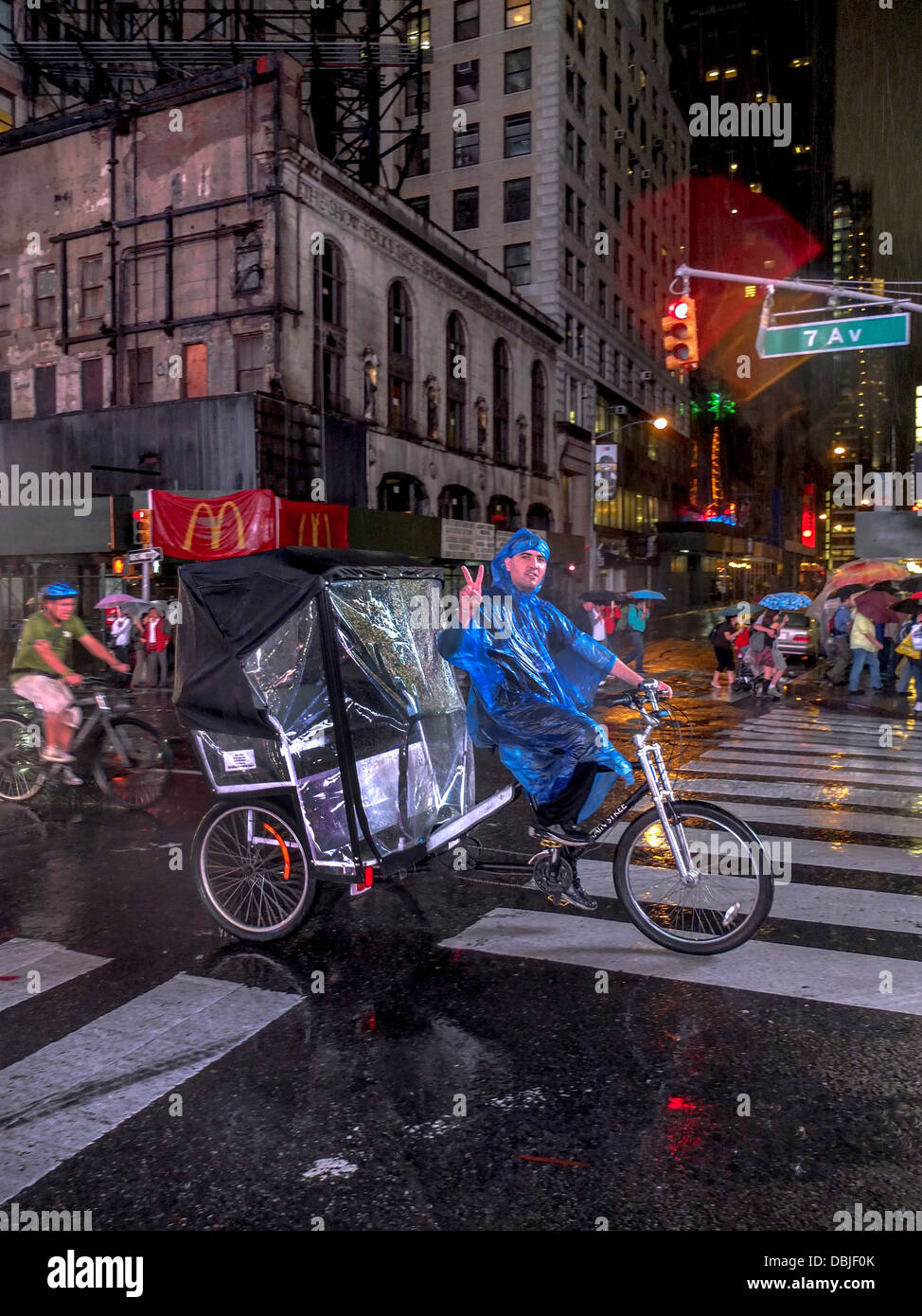 Un ispanica raincoated pedicab taxi driver onde una V-segno anche durante la corsa verso il basso Broadway in Times Square a New York City Foto Stock