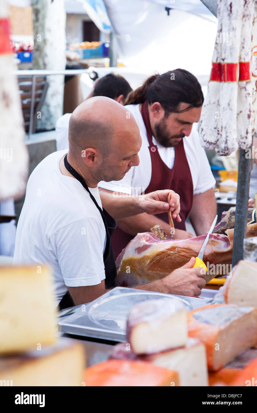 Commerciante carving Palma prosciutto alla Città Vecchia Pollensa mercato di Domenica in la principale piazza di Plaza Mayor e. Foto Stock