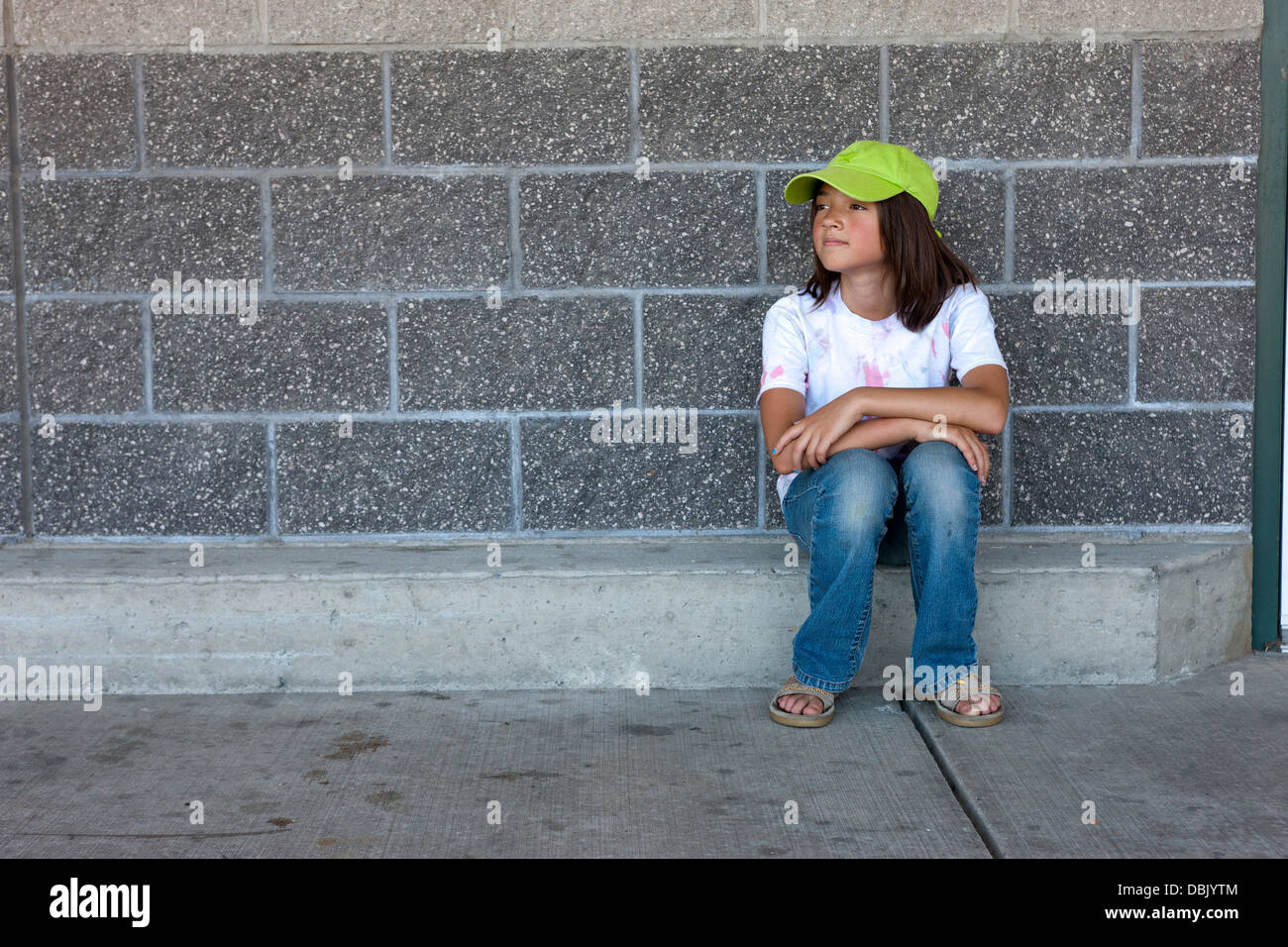 Una giovane ragazza si siede su un piccolo passo di fronte a un muro di mattoni. Foto Stock