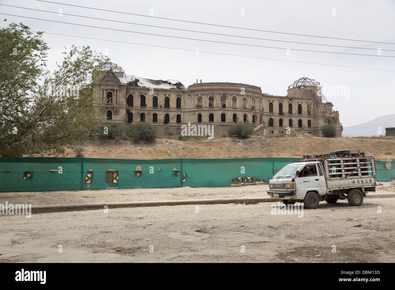 Afghan uomo cinese di guida carrello con bombole di gas passato le rovine di Darul Aman Palace, Kabul, Afghanistan Foto Stock