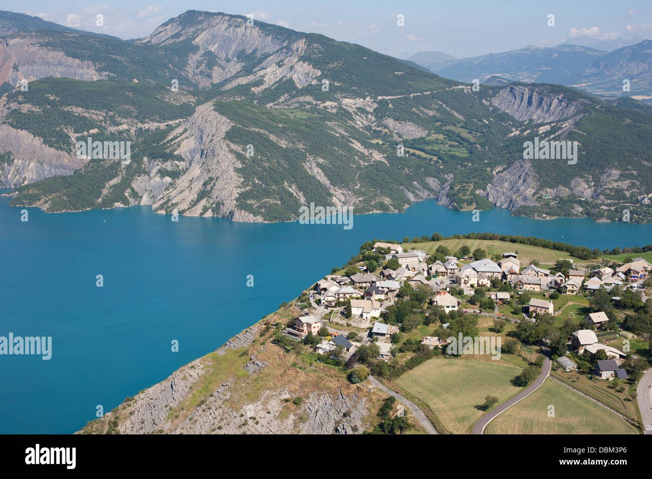 VISTA AEREA. Piccolo villaggio con una vista raccomandabile del lago Serre-Poncon 250 metri sotto. Le Sauze-du-Lac, Hautes-Alpes, Francia. Foto Stock