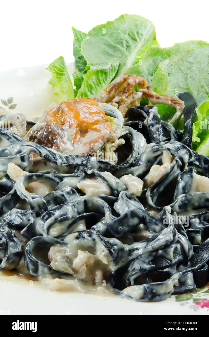 Close up tagliatelle nere (pasta fatta con nero di seppia) con sugo alla carbonara , granchi fritti e verdura fresca sulla piastra Foto Stock