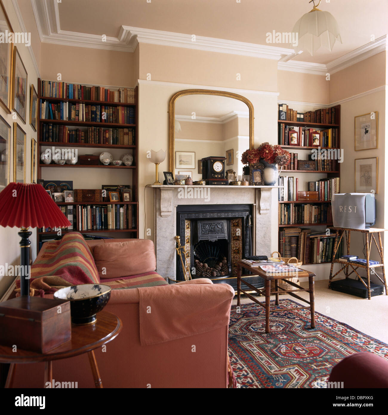 Rosa scuro divano in stile vittoriano stanza vivente con specchio dorato  sopra caminetto in marmo tra alcove a scaffali Foto stock - Alamy
