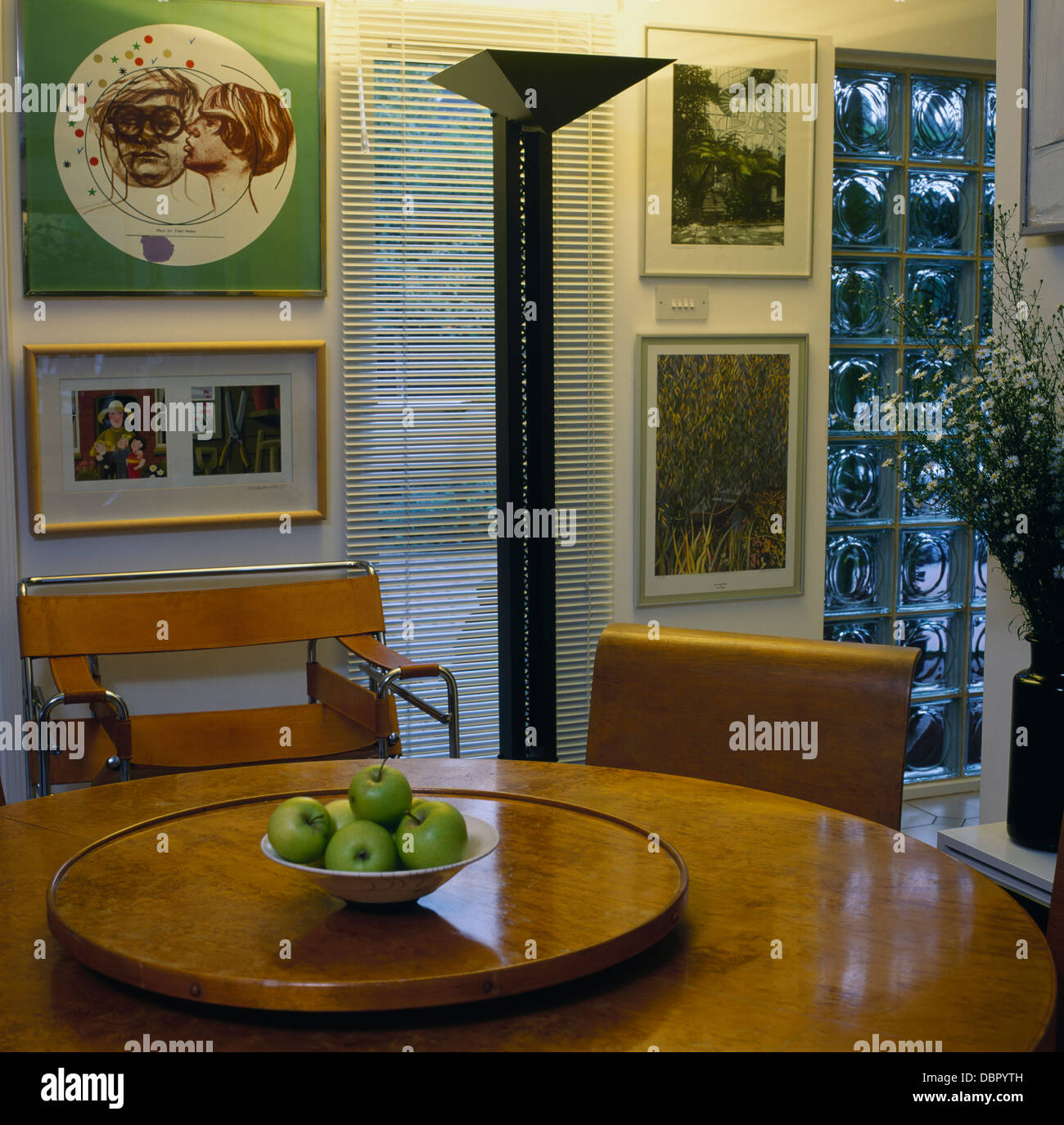 Lampada da terra accanto a Breuer sedia a tavola con Lazy Susan nella moderna sala da pranzo con gruppo di dipinti e vetro di finestra di mattoni Foto Stock