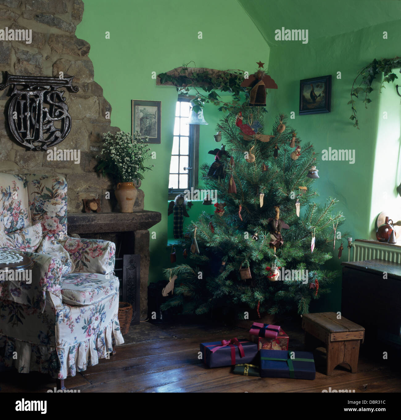 Albero di natale in un angolo di verde cottage soggiorno con pavimento in legno e poltrona floreale Foto Stock