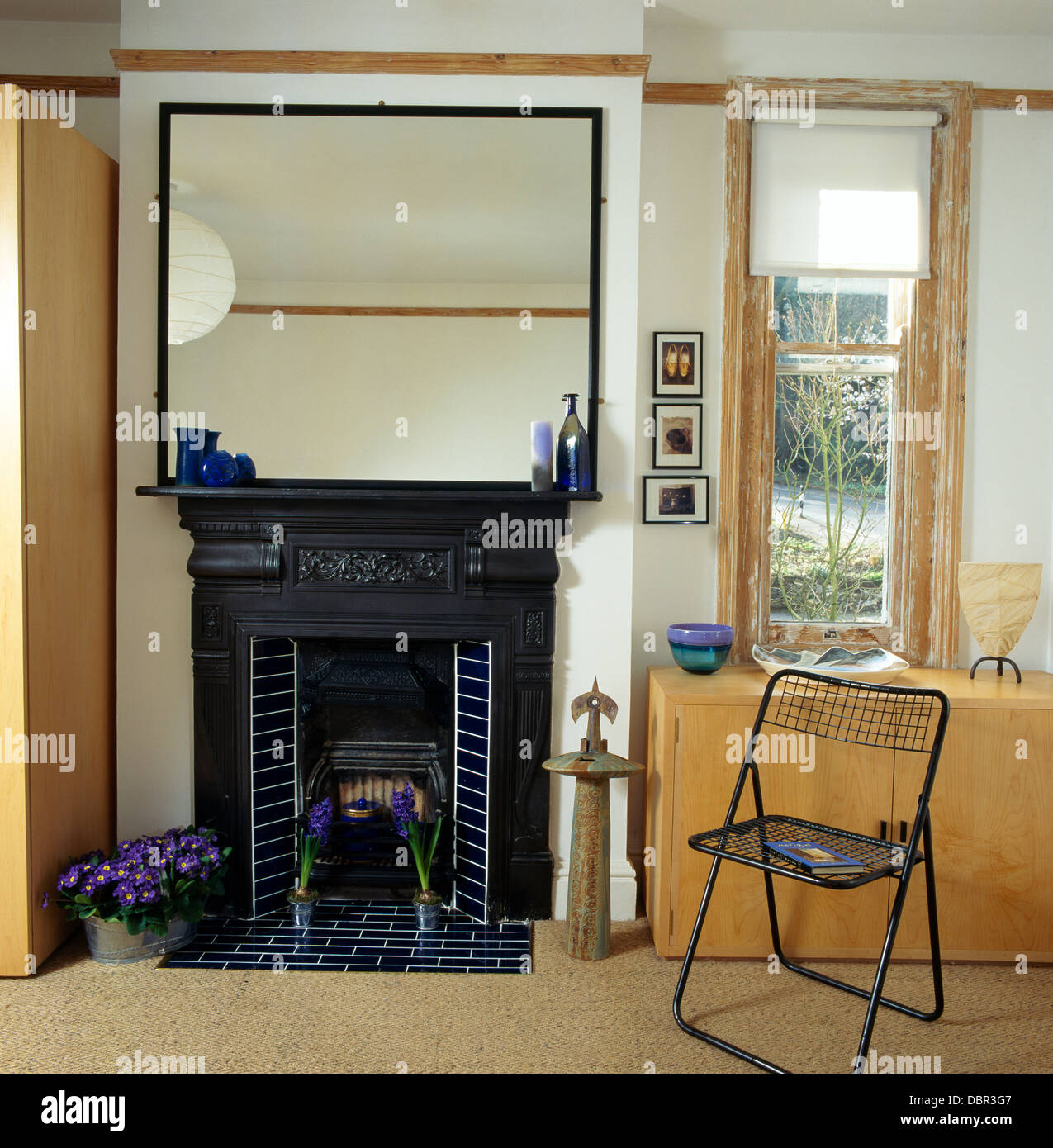 Grande specchio sopra il nero ghisa Edwardian caminetto nella sala da pranzo moderna con sedia in metallo e finestra stretta con tenda bianca Foto Stock