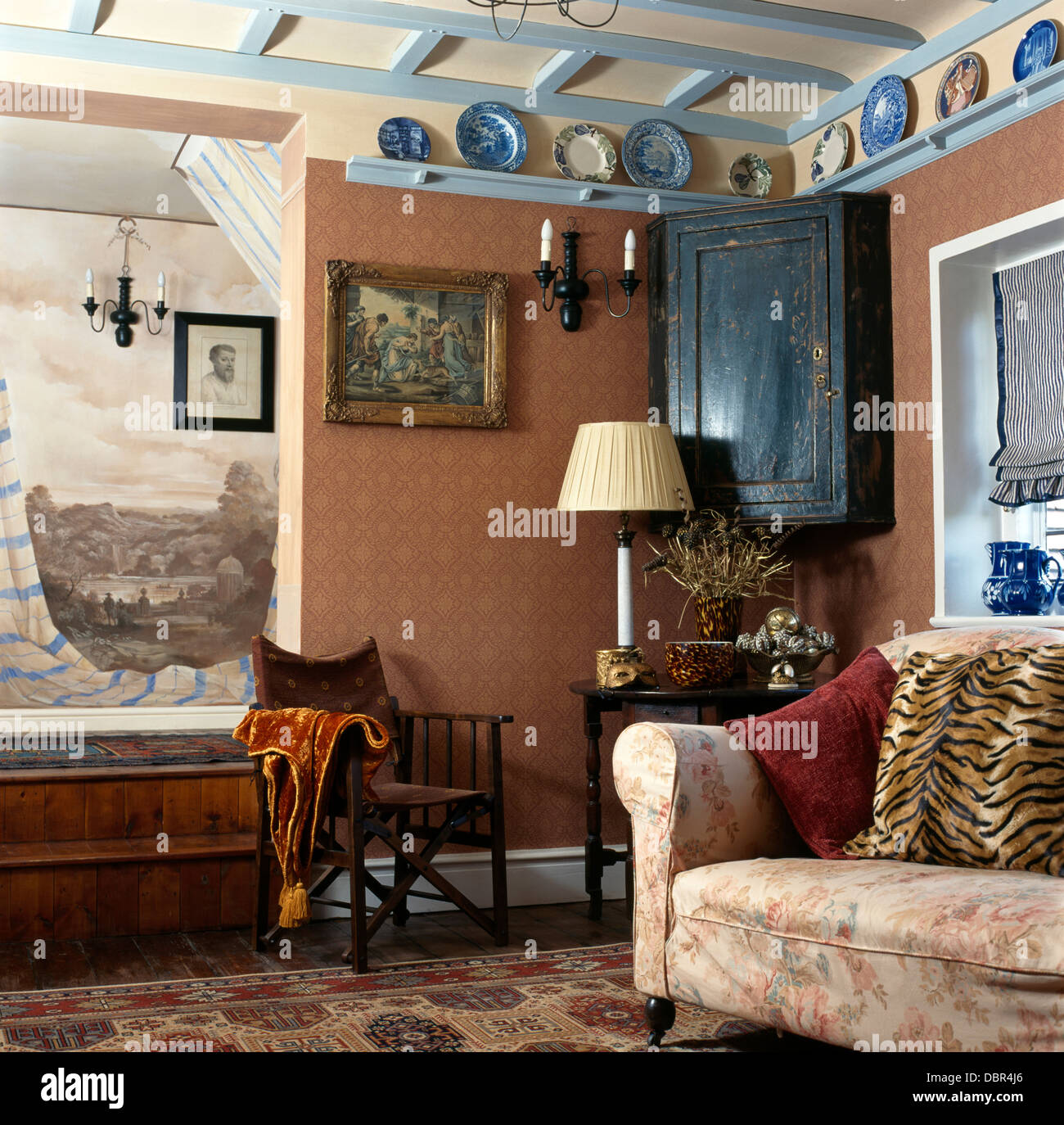 Dipinto murale sopra legno scuro del direttore della cattedra in rosa cottage soggiorno con angolo antica credenza e blu+soffitto bianco Foto Stock