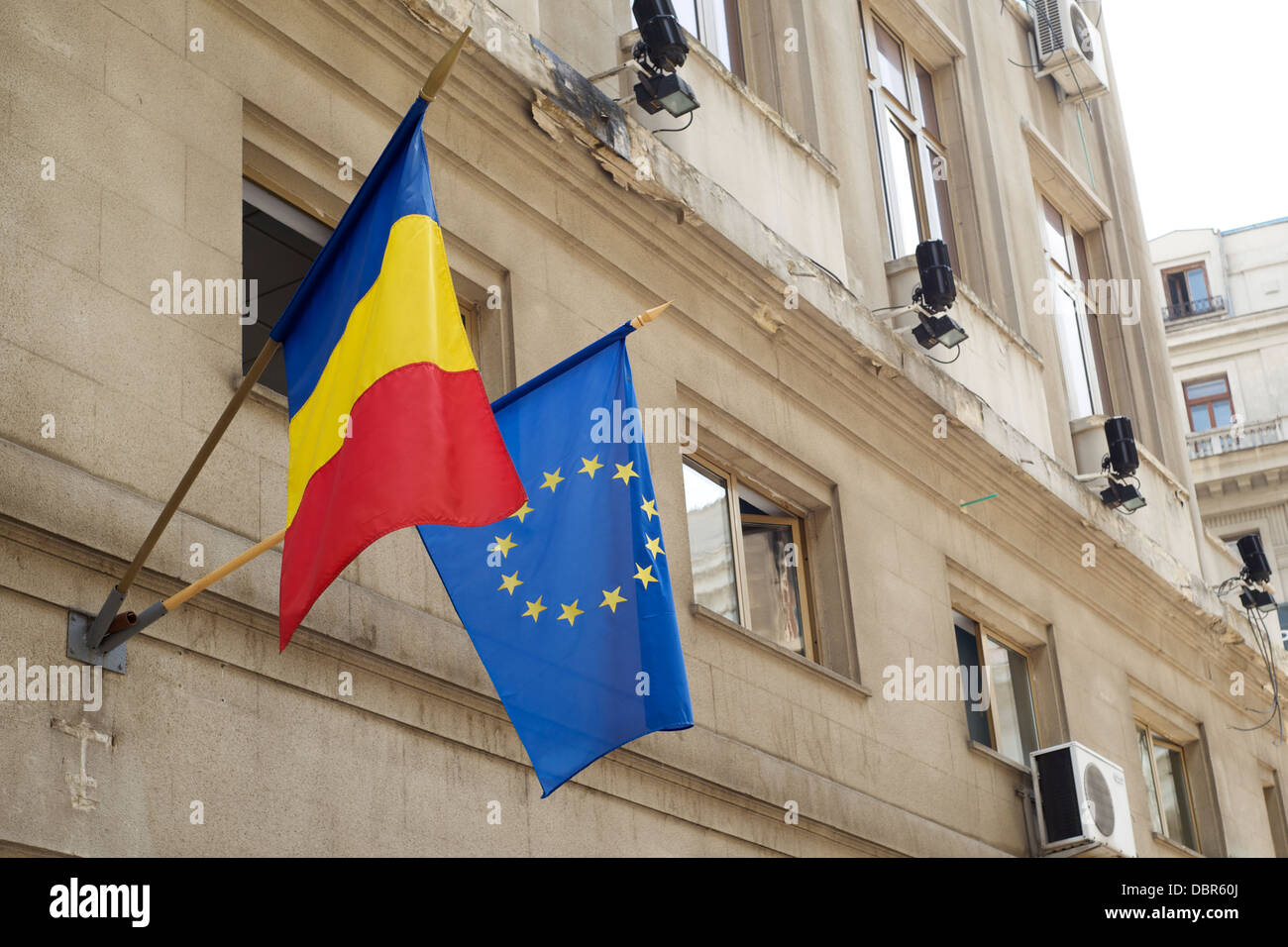 Ue e bandiere rumene pendenti da poli all'esterno di un edificio Foto Stock