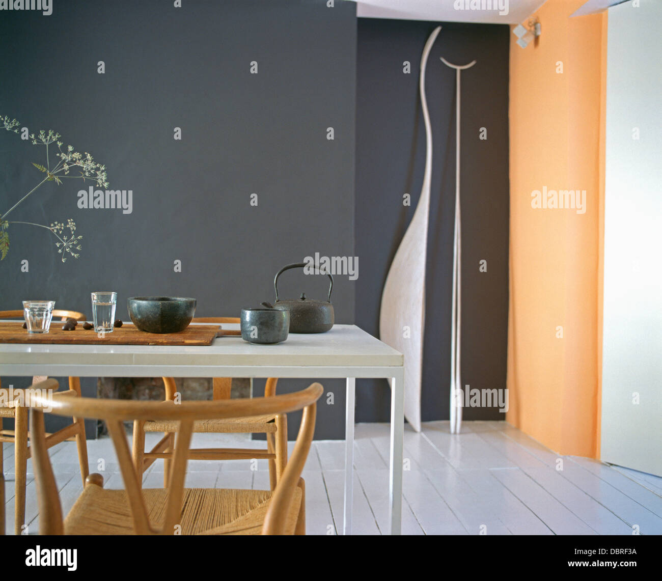 Sedie in legno a tavola con nero teiera e bocce in nero sala da pranzo moderna con dipinti di bianco Assi di pavimento e muro arancione Foto Stock
