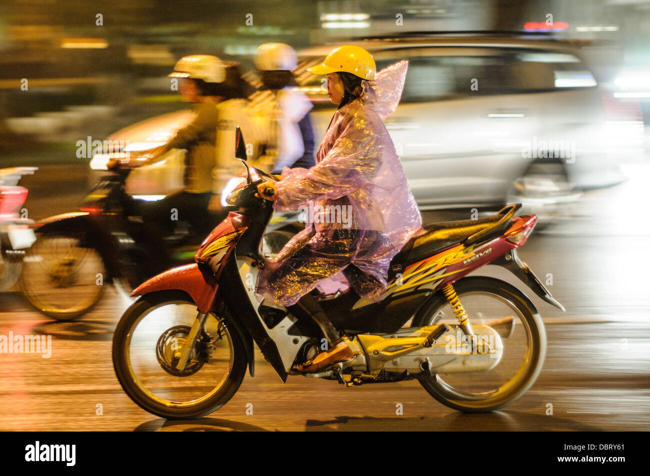 HANOI, Vietnam - Una donna in moto negozia il traffico frenetico del centro storico di Hanoi di notte sotto la pioggia. Foto Stock