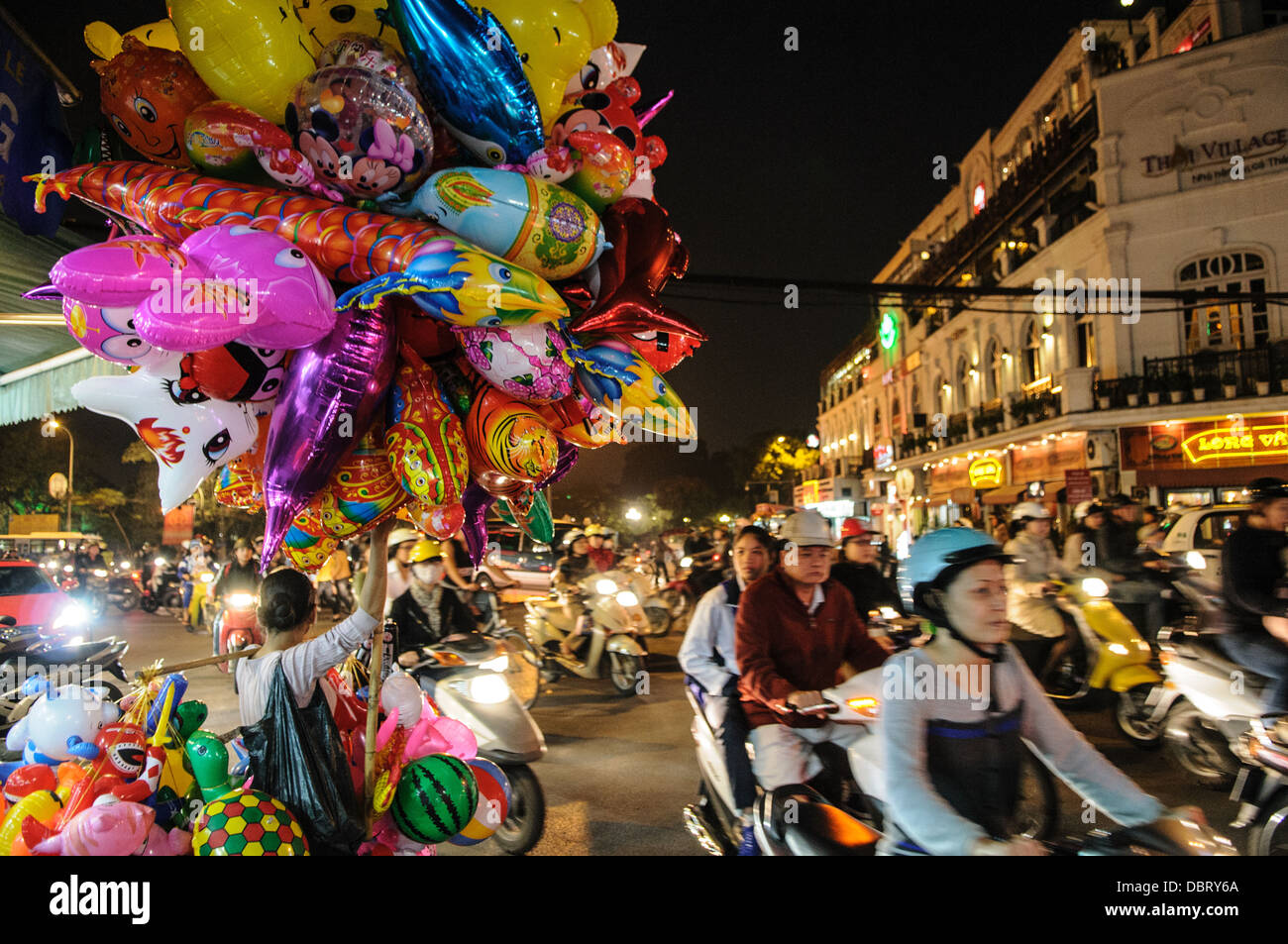 HANOI, Vietnam: Traffico intenso su biciclette e scooter di notte nel quartiere vecchio di Hanoi. A sinistra un venditore di palloncini vende i suoi prodotti. Foto Stock