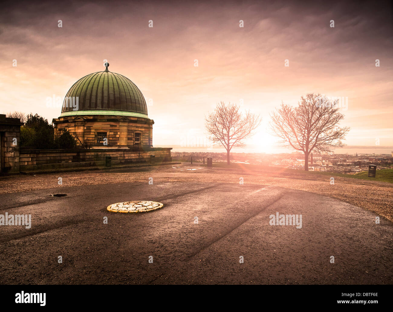 Edificio a cupola e Calton Hill, Edimburgo. Ci sono due alberi sfrondato e il sole tramonta all'orizzonte Foto Stock