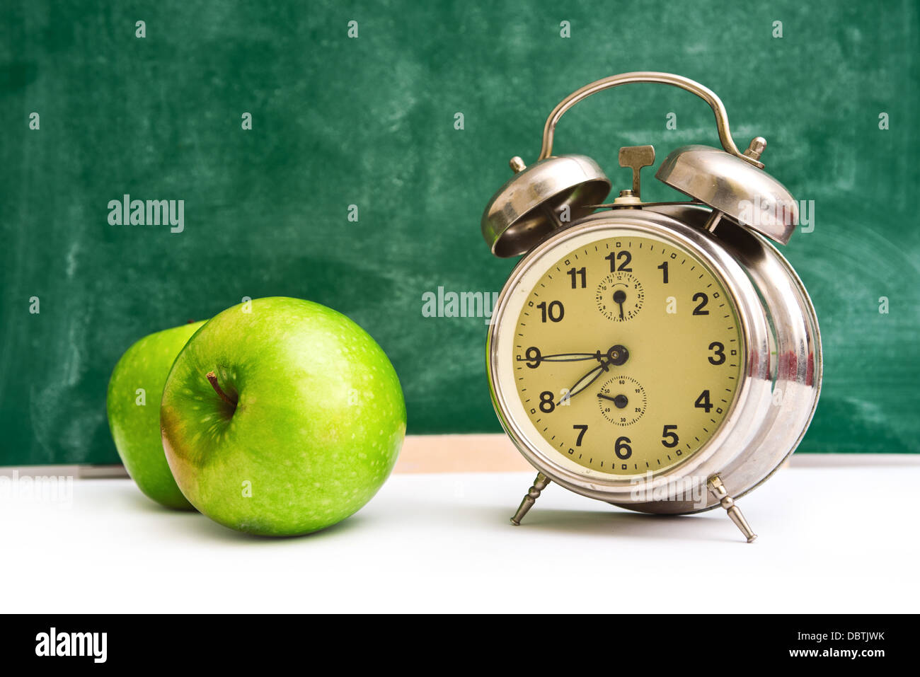 Scuola di nuovo tempo. Orologio e mele sul maestro del tavolo, lavagna verde in background. Si torna a scuola. Foto Stock