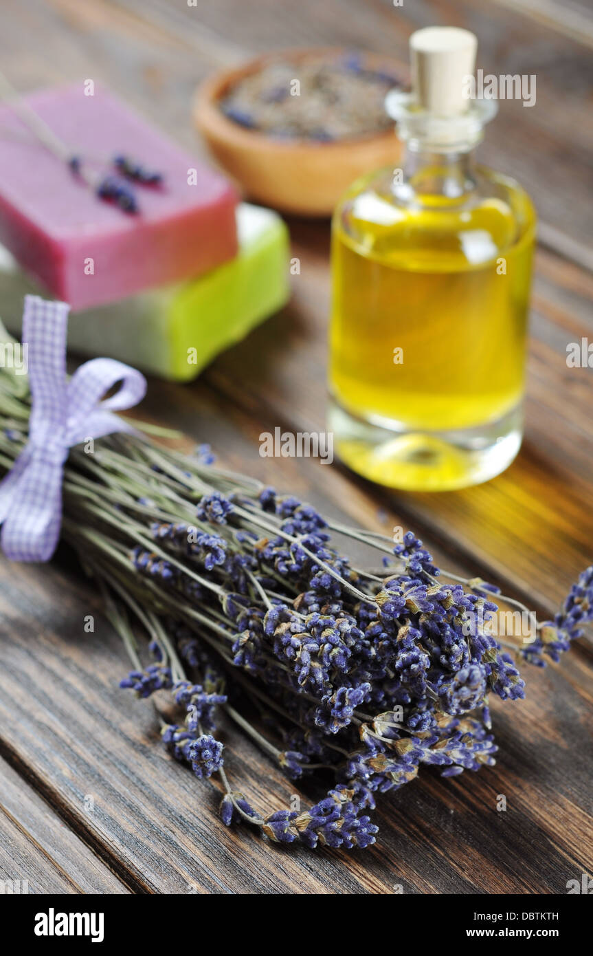 Essenziale di olio di lavanda, sapone a base di erbe e mazzo di fiori di lavanda su sfondo di legno. Foto Stock