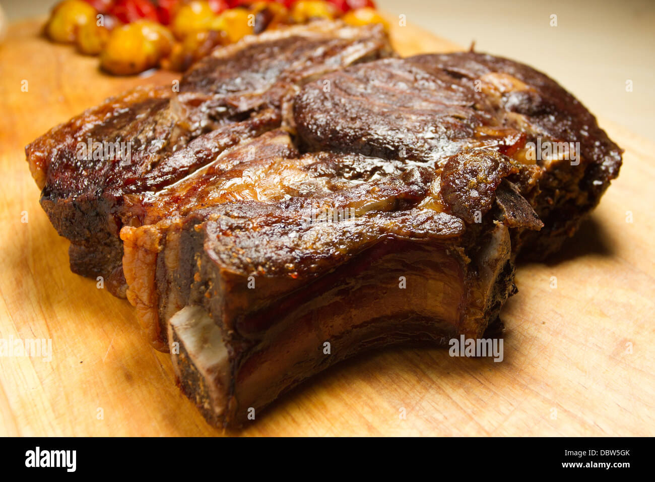 Costola arrosto di carne su un tagliere di legno, con arrosti di carne rossa e pomodori giallo Foto Stock