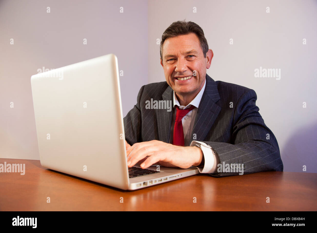 Uomo d'affari a una scrivania utilizzando un computer portatile, guardando la telecamera sorridendo. Foto Stock