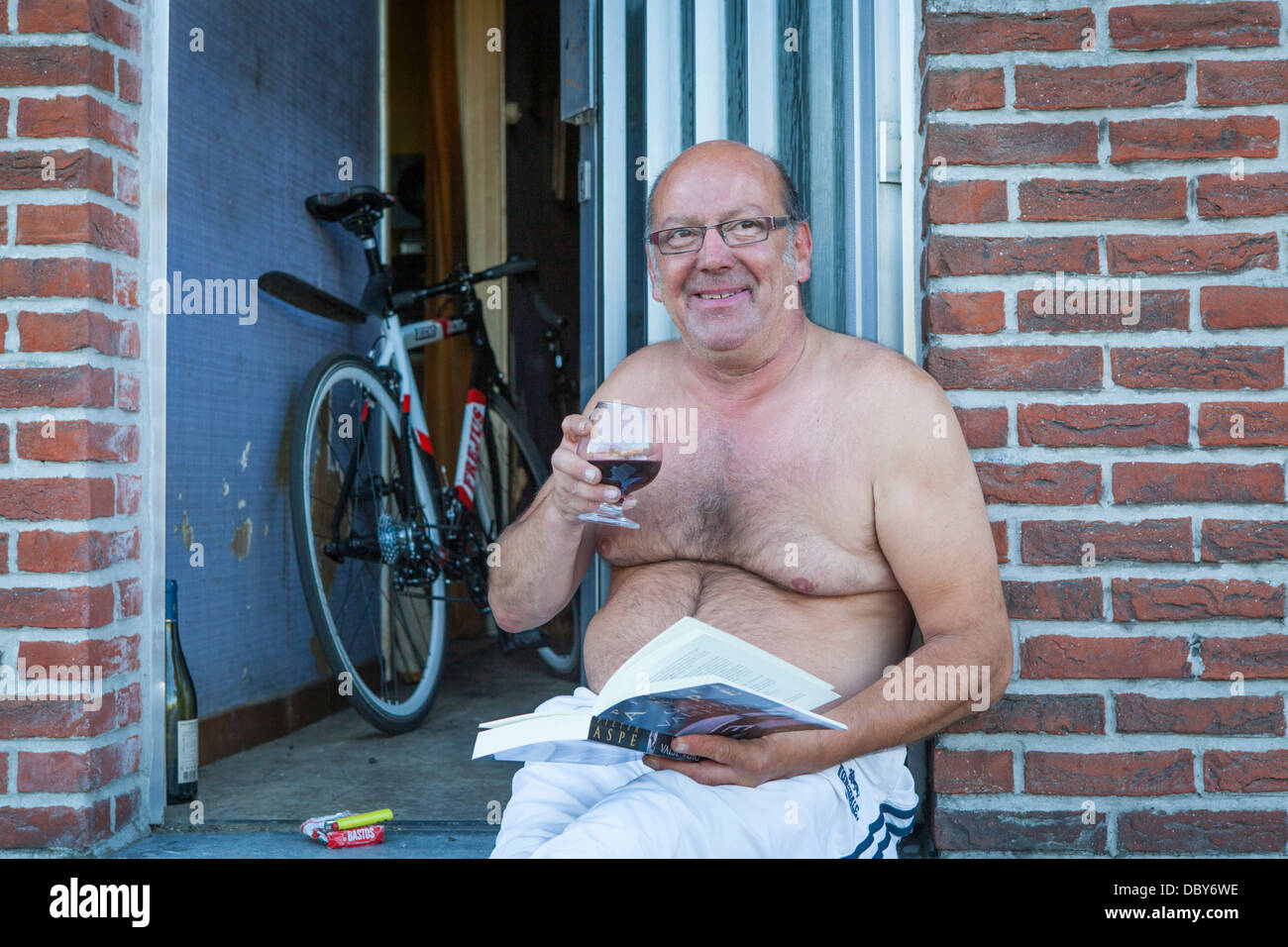 Uno degli ultimi abitanti del villaggio abbandonato di Doel leggendo un libro e avente un bicchiere di vino rosso nella sua porta Foto Stock