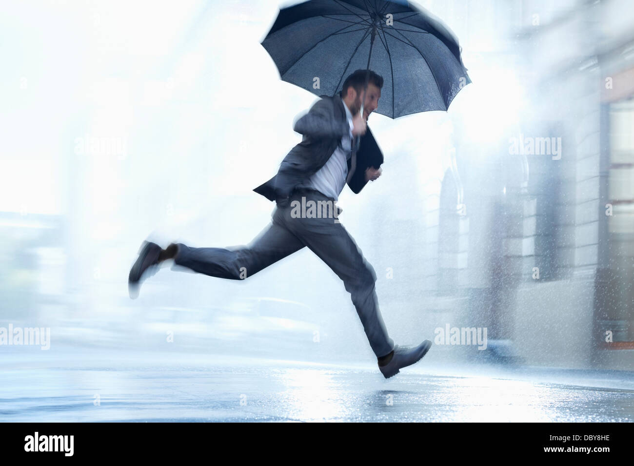 Imprenditore in esecuzione con ombrello in rainy street Foto Stock
