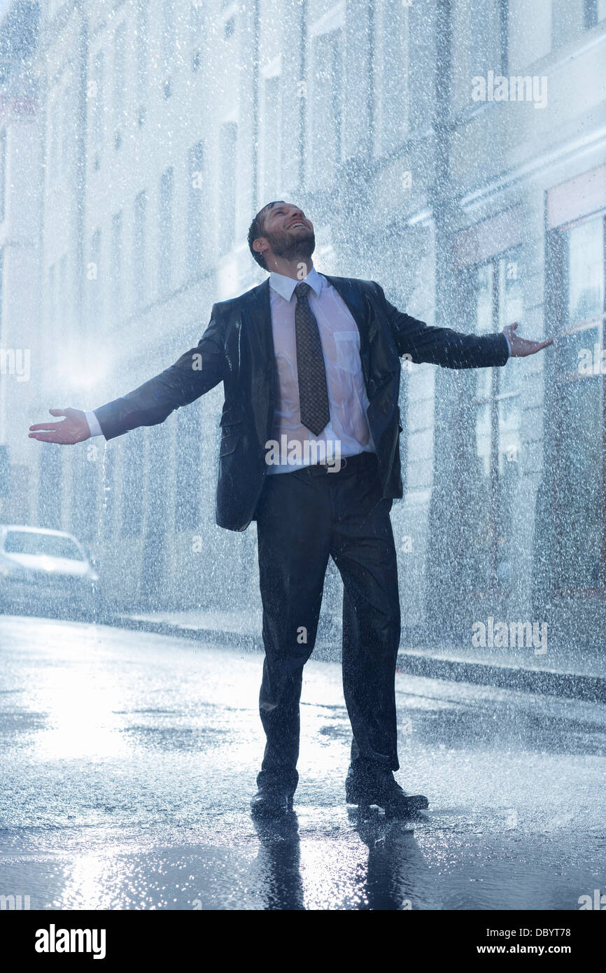 Imprenditore in piedi con le braccia tese in rainy street Foto Stock
