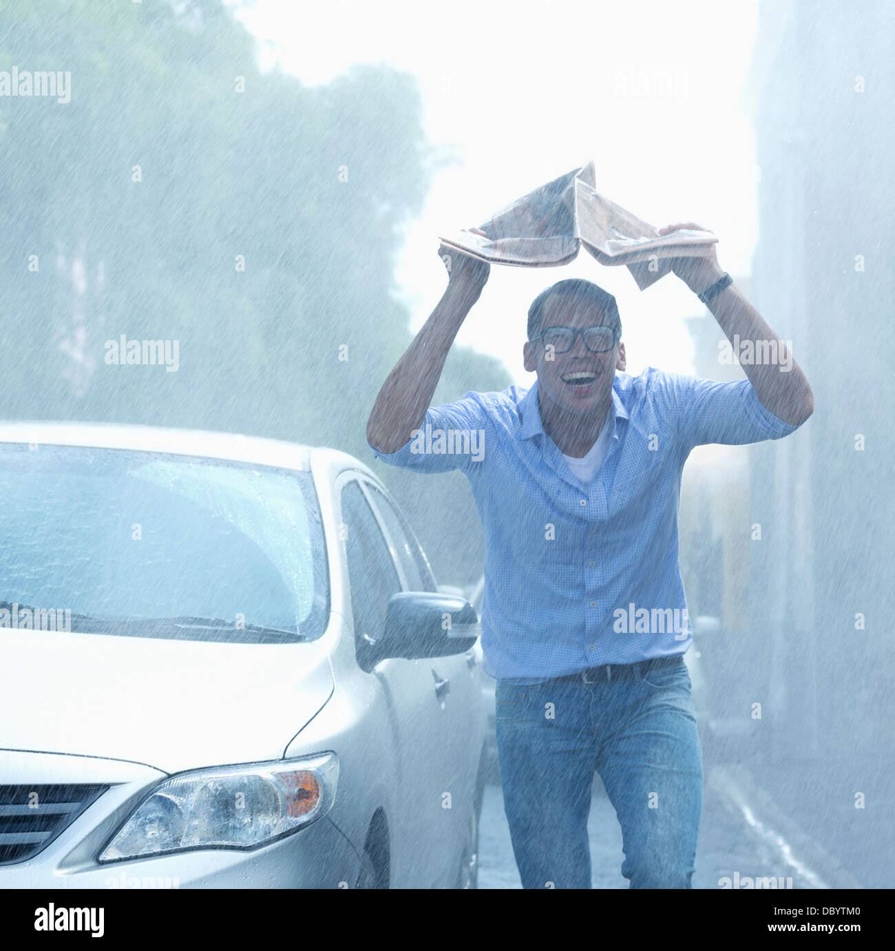 Uomo sorridente azienda giornale overhead in rainy street Foto Stock